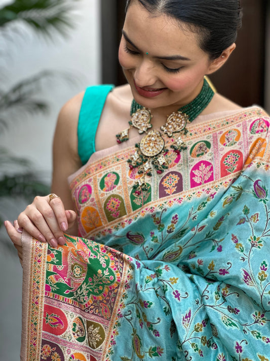 Woman wearing a colorful saree with intricate patterns, holding it in front of her. Indraneel Meenakari Jacquard Floral Saree for Women | Yuvani Vesture