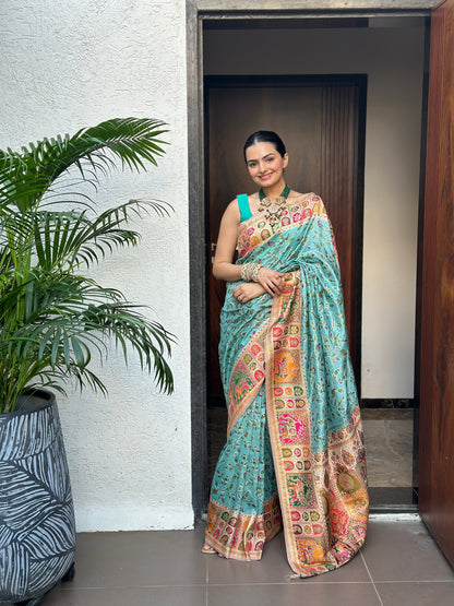 Woman in a colorful saree standing in a doorway with a plant to her left. Indraneel Meenakari Jacquard Floral Saree for Women | Yuvani Vesture