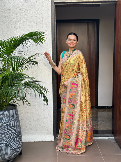 Woman in a traditional saree standing in a doorway with plants in the foreground. Peetambari Meenakari Jacquard Floral Print Saree | Yuvani Vesture