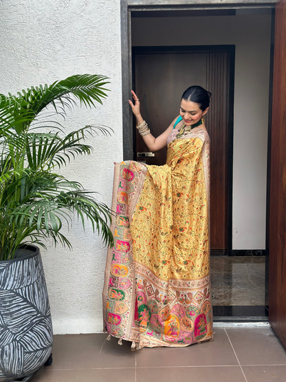 Woman holding a large folded saree with a decorative pattern in a room. Peetambari Meenakari Jacquard Floral Print Saree | Yuvani Vesture