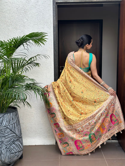 Woman holding a traditional saree in a room with plants and furniture. Peetambari Meenakari Jacquard Floral Print Saree | Yuvani Vesture