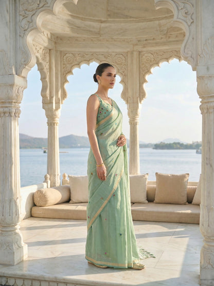 Woman in a light green saree standing in front of an archway with a scenic view. Pista Green Jamdani Cotton Saree