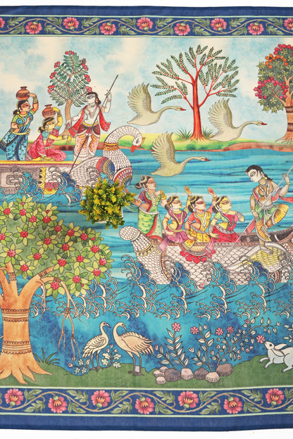 A detailed image of a Tarangini Chanderi saree with a depiction of Krishna's river journey, showing multiple characters, birds, and a floral pattern against a blue background. Tarangini Chanderi Saree | Yuvani Vesture